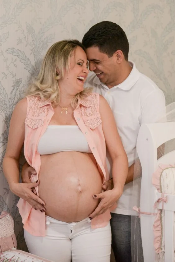 Gledson e Keila sorriem abraçados; ela está grávida.
